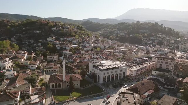 Aerial cityscape of Berat with historic King Mosque and the Lead Mosque, surrounded by traditional Ottoman houses and modern buildings against a backdrop of hazy mountains
