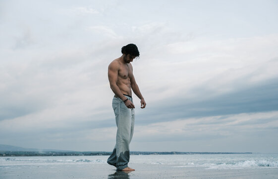 Man with muscular physique standing on a wet beach with ocean waves in the background
