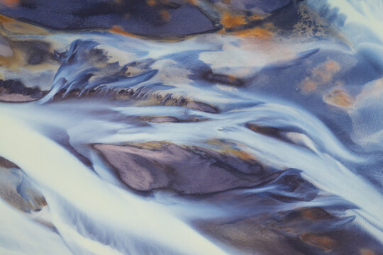 Aerial view of a braided glacial river with silvery water flowing through dark volcanic sand and orange sediment Iceland.
