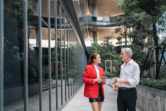 Business meeting office building outdoor man woman conversation urban glass window walkway professional red blazer white shirt business attire teamwork communication corporate workplace modern
