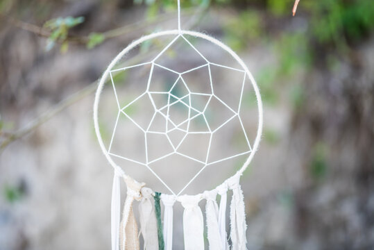 White Handmade Dreamcatcher Hanging Outdoors with Soft Bokeh Nature Background
