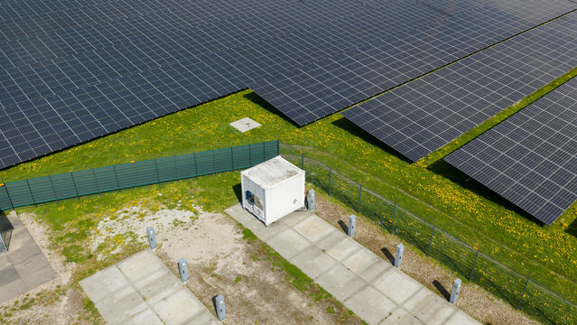 Aerial view of solar panels in a large array on a green field with yellow wildflowers and a white technical building Warmenhuizen, North Holland, Netherlands.
