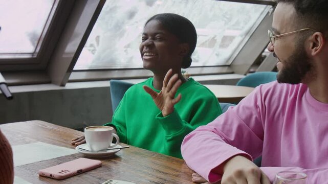 Joyful African American girl laughing during funny conversation with friends while visiting restaurant at weekend