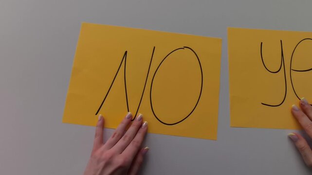 Close-up of a woman&rsquo;s hands sliding two paper cards labeled &ldquo;Yes&rdquo; and &ldquo;No&rdquo; across a table, finally leaving &ldquo;Yes&rdquo; in place. Minimal, clean visual illustrating decision-making, choice, and positive outc