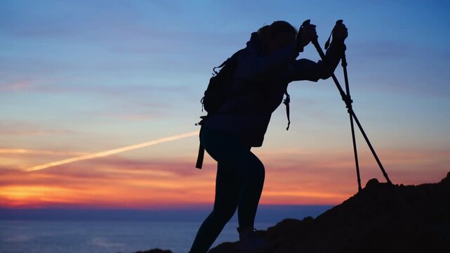 Silhouette of female hiker with trekking poles climbing mountain peak at dawn.Concepts of perseverance, goal achievement and outdoor adventure