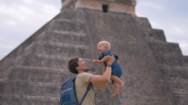 Happy father throwing his one year old son into the air in front of Kukulkan pyramid in Chichen Itza, Mexico. Family travel, joy, bonding and unforgettable vacation moment concept. Slowmotion video.