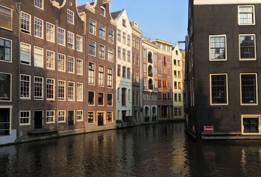 Colorful traditional buildings reflecting in the canal water in Amsterdam, Netherlands. Classic Dutch architecture illuminated by soft evening sunlight