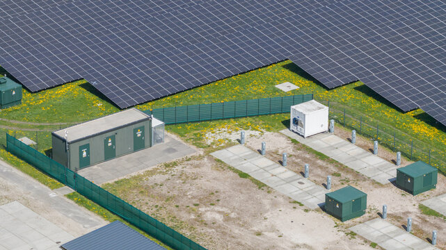 Aerial view of a large solar farm with rows of photovoltaic panels, technical containers, and green grass with yellow flowers Warmenhuizen, North Holland, Netherlands.