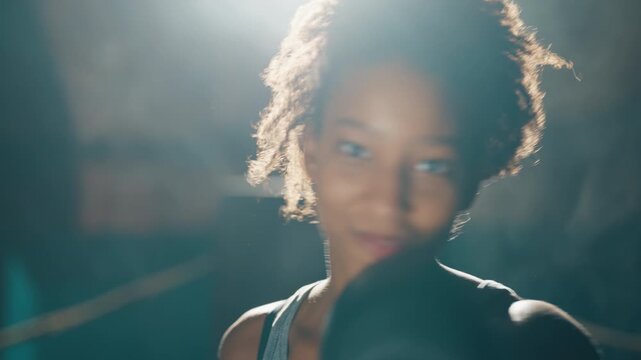 Motivated african woman boxing and punching by hands to camera, portrait shot. Attractive sportswoman training on box ring, professional fighter, self-defense and aggression release, emotional face