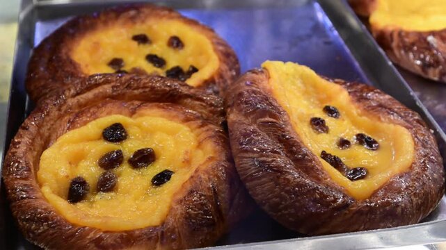 Delicious baked pastries with custard cream and raisins displayed on a metal tray in a patisserie shop window, a perfect treat for a sweet breakfast or snack, showcasing italian culinary tradition