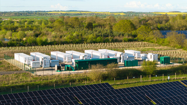Aerial view of Tiln Photovoltaic Solar Farm and Battery Energy Storage System with white storage containers and solar panels surrounded by lush green trees in Retford, England, United Kingdom.