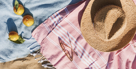 Obraz premium Summer beach accessories flat lay on sand background. Holiday travel, tropical concept. Straw hat, sunglasses, towel and fruits. Sun shadow and sunlight