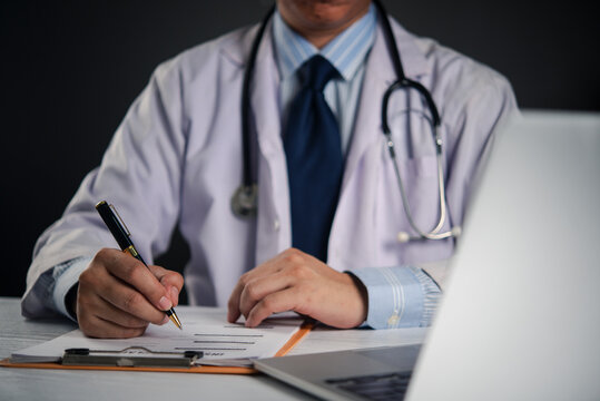 Healthcare provider authorizing medical document pen clipboard desk blurred laptop foreground hospital workflow physician order entry compliance record.