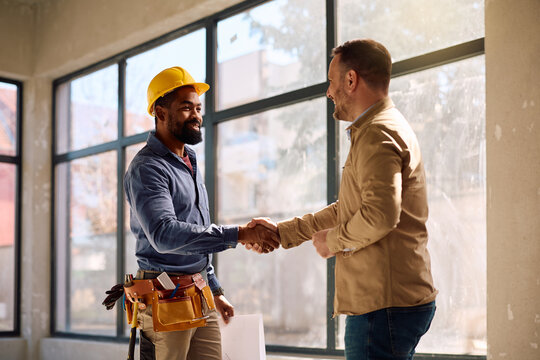 Happy African American worker handshaking with his client at construction site.