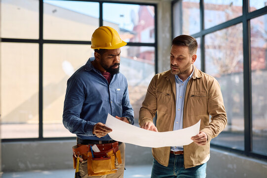 Black worker and his client analyzing house remodeling plans at construction site.