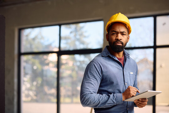 Black worker with touchpad at construction site looking at camera.