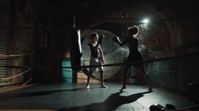 Professional sport and healthy lifestyle, self-defense class for women in gym. Intensive cardio workout, female fighter practicing arms punches, workout with coach, african american sportswoman