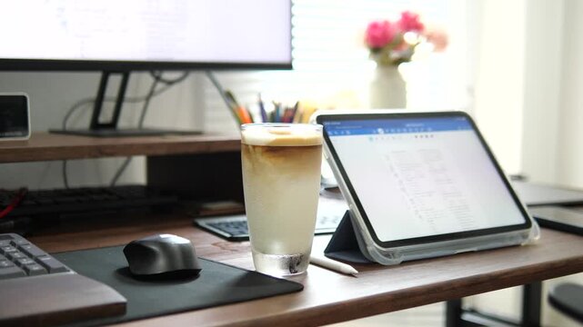 Cinematic close-up of a layered iced latte coffee in a glass with a blurred computer monitor background, modern office and remote work lifestyle concept