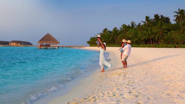 A happy holiday family is having fun on a tropical beach in the Maldives islands during sunset time