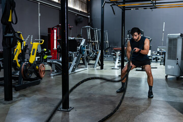 Fototapeta premium Young man working out with battle ropes in gym determination, strength and endurance Training Concept, l athlete performing battle rope exercise at the gym intensity and healthy routine.