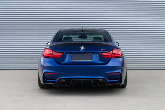 Blue BMW M4 full centered rear view, Performance coupe sportscar outdoors in front of metal wall