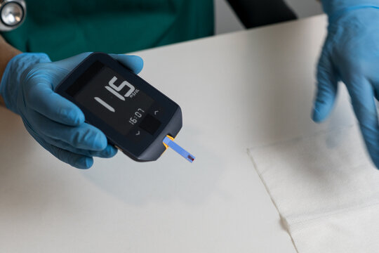 A close-up of a hand holding a glucometer showing a blood sugar reading of 115 mg/dL with a test strip inserted.