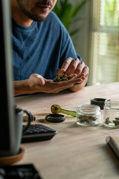 Man choosing cannabis buds, with cannabis equipment and accessories on the table