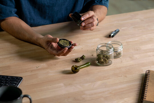 Man using cannabis grinder, with cannabis equipment and accessories on the table.