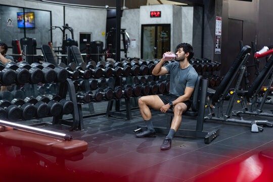 Athletic Man Drinking Protein Shake After Workout in Modern Gym. Male Athlete Recovering with Protein Drink During Workout Gym Break.