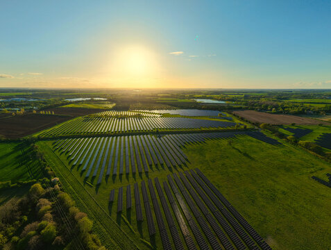 Aerial view of the Tiln Photovoltaic Solar Farm and Battery Energy Storage System with rows of solar panels across green fields at sunset Retford, England, United Kingdom.