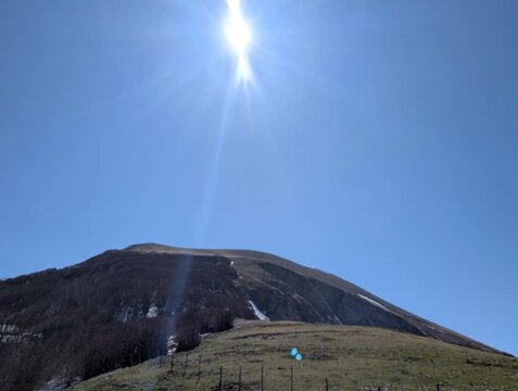   
Panoramica luminosa di un paesaggio montano con sole alto, pendii erbosi e recinzione in primo piano. Atmosfera naturale, ampia e ariosa