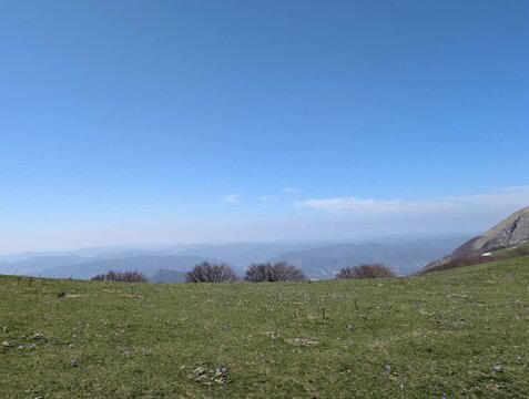   
Ripresa panoramica di una montagna verde con arbusti e montagne sullo sfondo, sotto un cielo limpido. Atmosfera naturale, luminosa e tranquilla