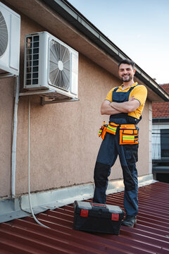 Hvac technician posing with arms crossed after installing an air conditioner on a rooftop