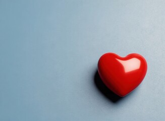 Fototapeta premium A single polished red heart object resting on a smooth light blue surface, featuring a soft shadow cast to the left and a clean minimalist aesthetic perfect for romantic themes and creative projects.