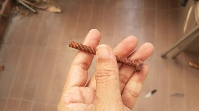 A person's hand holds and rotates a long, heavily rusted hex head iron bolt, showing deep corrosion and orange rust texture from old age.