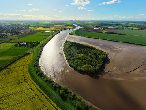 Aerial view of Howden Dyke Island in the River Ouse surrounded by lush green and yellow rapeseed fields under a blue sky Goole, England, United Kingdom.