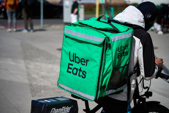 Uber Eats food delivery courier riding an electric bicycle on a sunny day along Grunwaldzka street, Gdansk, Pomerania, Poland, Europe.