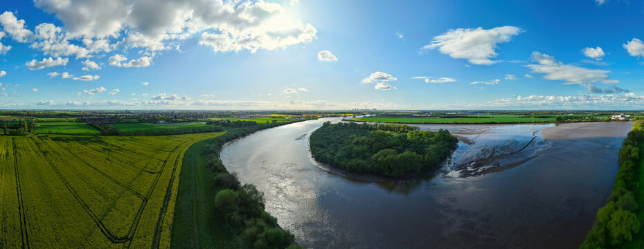 Aerial view of Howden Dyke Island in the River Ouse surrounded by yellow rapeseed fields and green meadows under a bright blue sky Goole, England, United Kingdom.