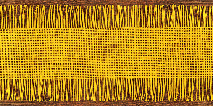 Woven yellow fabric rests on a brown surface displaying a pattern and texture in close view during daylight hours