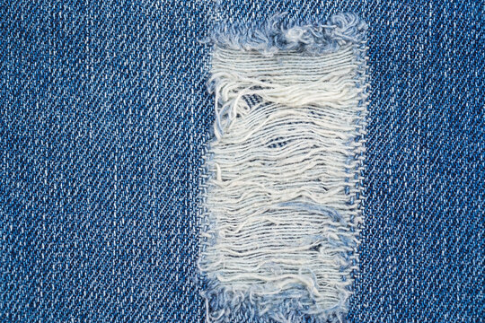 Denim fabric with torn area showing threads in blue color close to a stitch line
