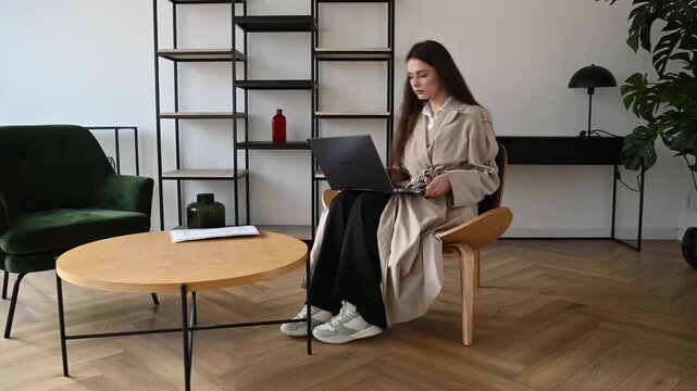 Focused young professional woman sitting in a modern chair while typing on her laptop computer, concentrating on her work project in a stylish and contemporary minimalist office interior