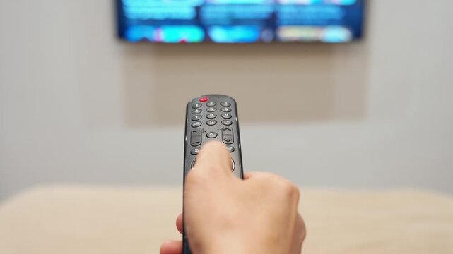 Close up of hand holding remote control and changing tv channels. Home entertainment and technology concept