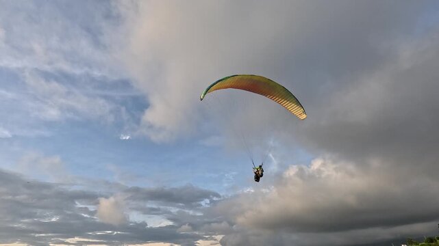Two people flying on a paraglider during a golden sunset.