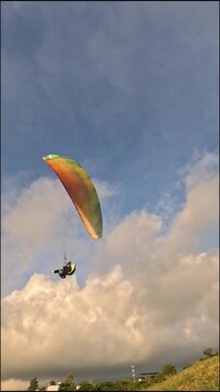 Vertical view of a paraglider flying with a colorful canopy at sunset.