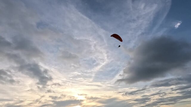 Paraglider silhouette flying through a vast sky with soft clouds at sunset