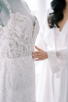 Gentle wedding prep. Soft morning glow illuminates bride smoothing gown with comforting presence nearby