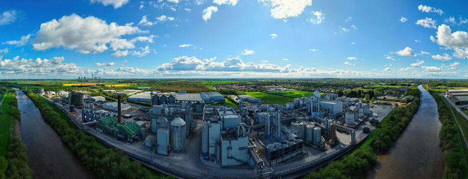 Aerial view of the Sedamyl Industrial Factory complex with large silos and processing units situated along the river under a bright blue sky with clouds in Selby, England, United Kingdom.