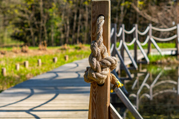 Naklejka premium Close-up of a thick natural fiber rope knot tied around a weathered wooden railing post, rustic architectural detail, texture of wood and cord, professional stock photo for construction or maritime.