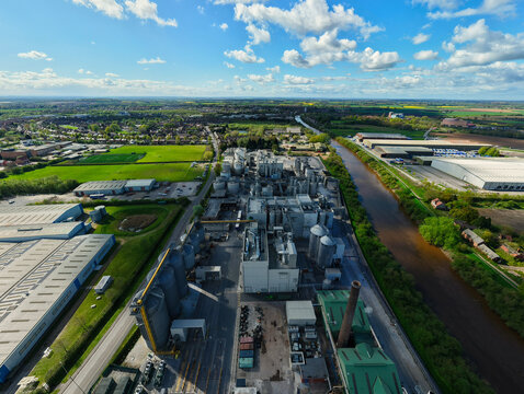 Aerial view of the Sedamyl Industrial Factory featuring large silos and complex machinery situated along a canal under a bright blue sky in Selby, England, United Kingdom.