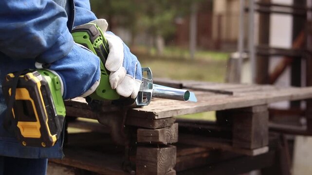 Cordless reciprocating saw cuts metal pipe. A craftsman in protective gloves uses a cordless reciprocating saw (electric knife) to saw a thin pipe. Working with a power tool. Close-up of work